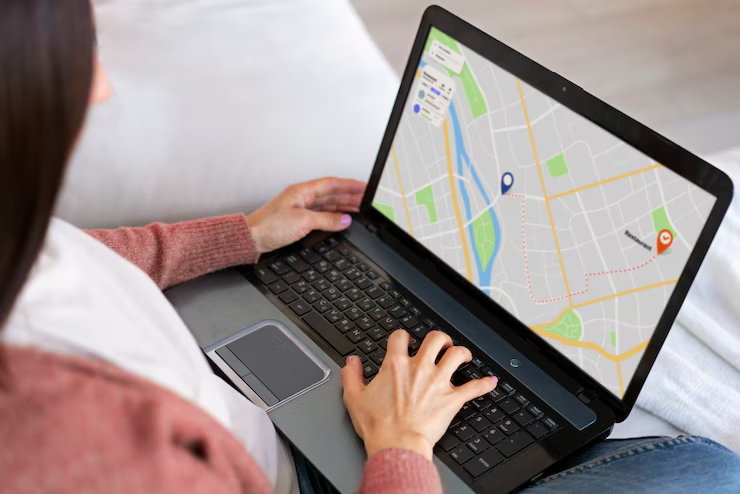 Person using laptop with map displaying navigation; setting on a bed.