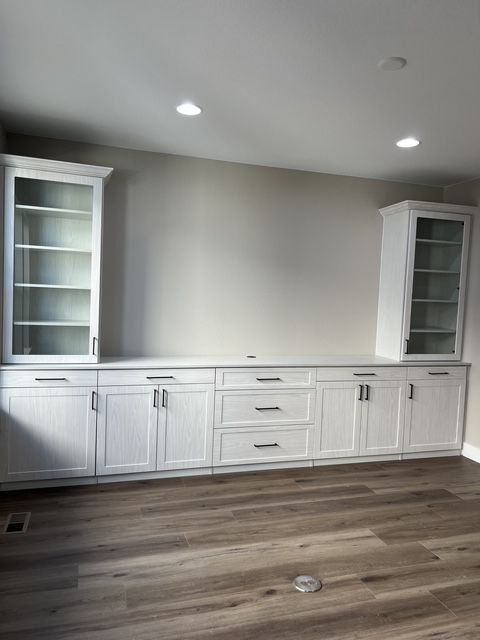 White built-in cabinetry with glass-door shelves, drawers, and cabinet doors against a neutral wall; hardwood floor.
