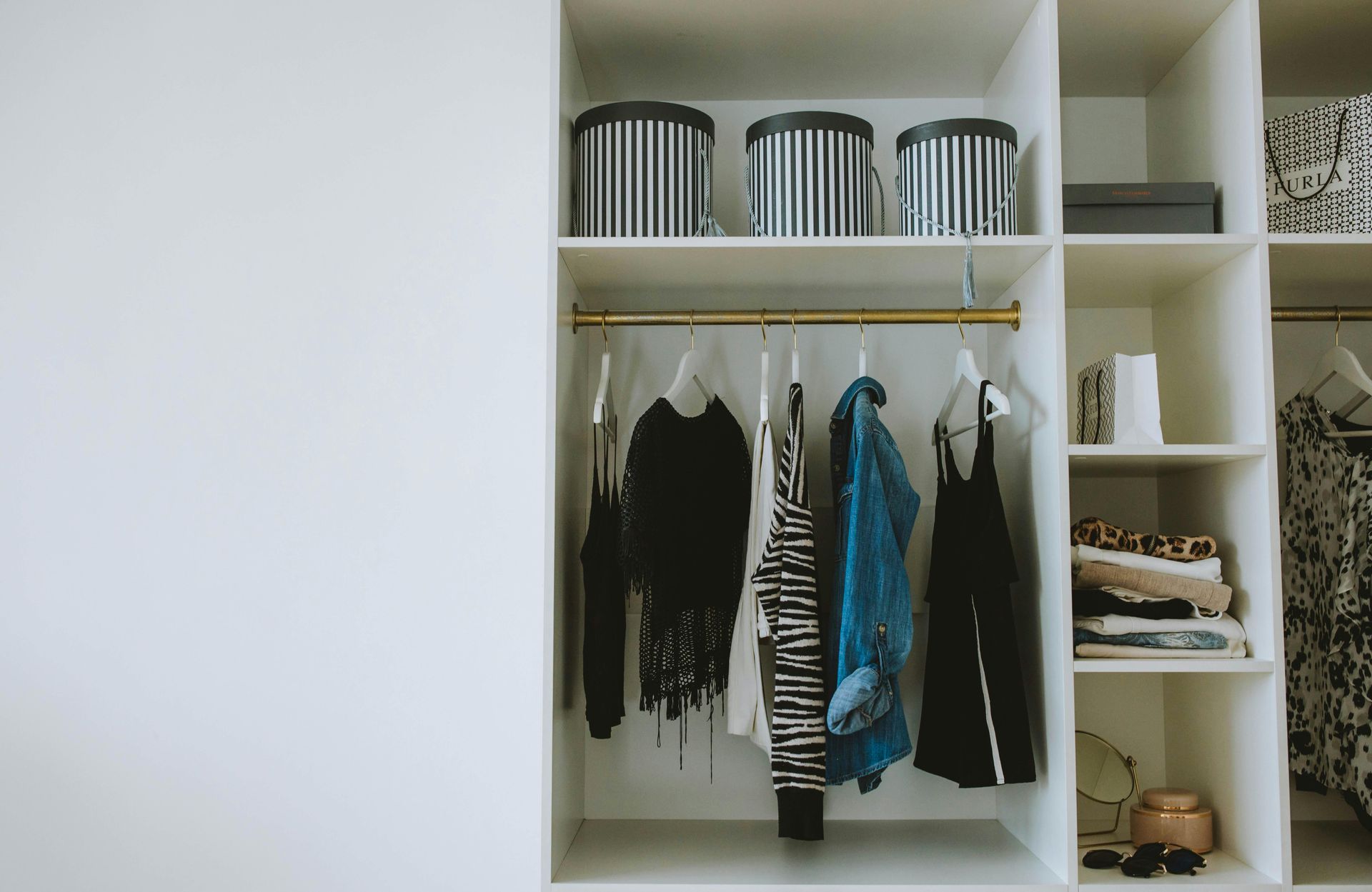 White closet with clothes hanging, storage boxes on top, and shelves.