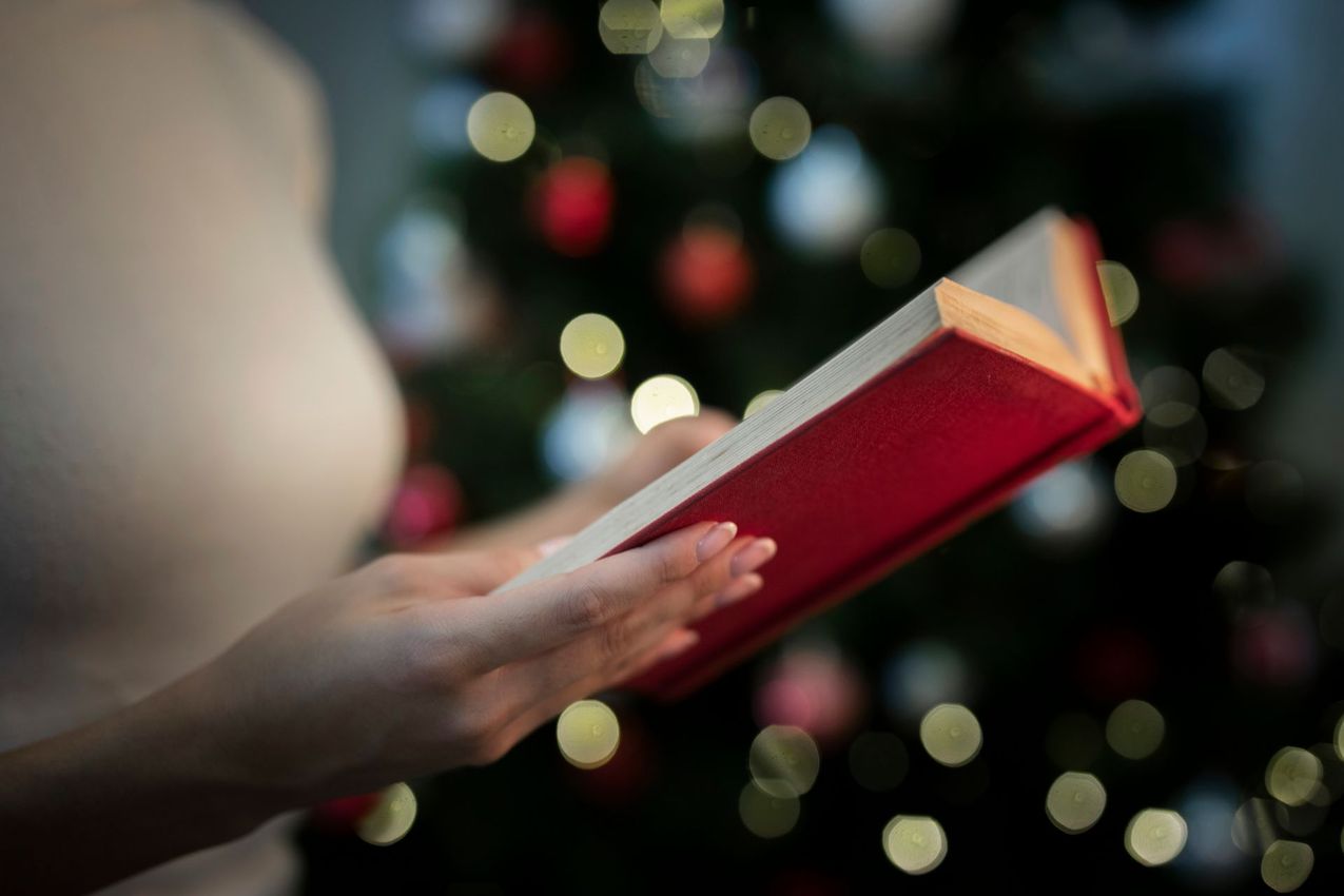 A woman is reading a book in front of a christmas tree.