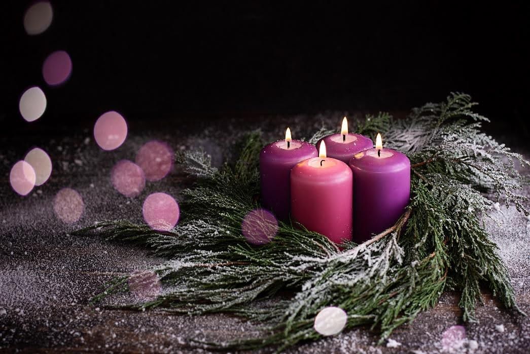 A wreath of purple candles and pine branches on a wooden table.