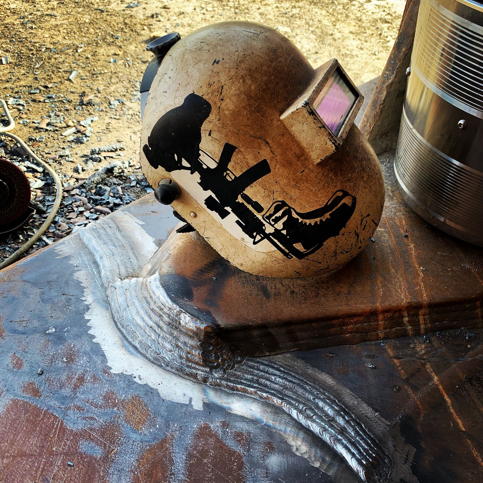Welding helmet with stickers rests on metal near a weld.