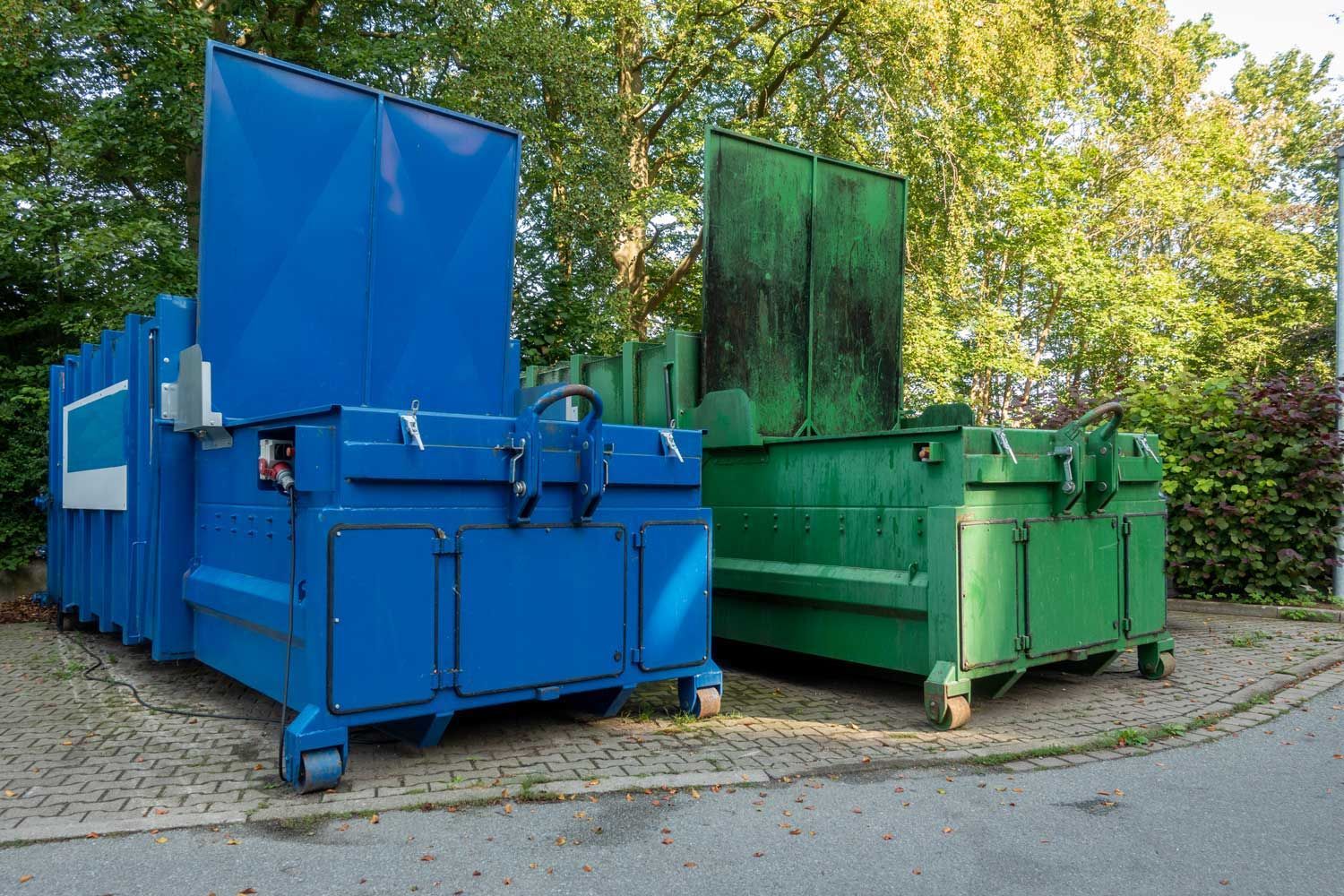 A blue dumpster and a green dumpster are parked next to each other on the side of the road.