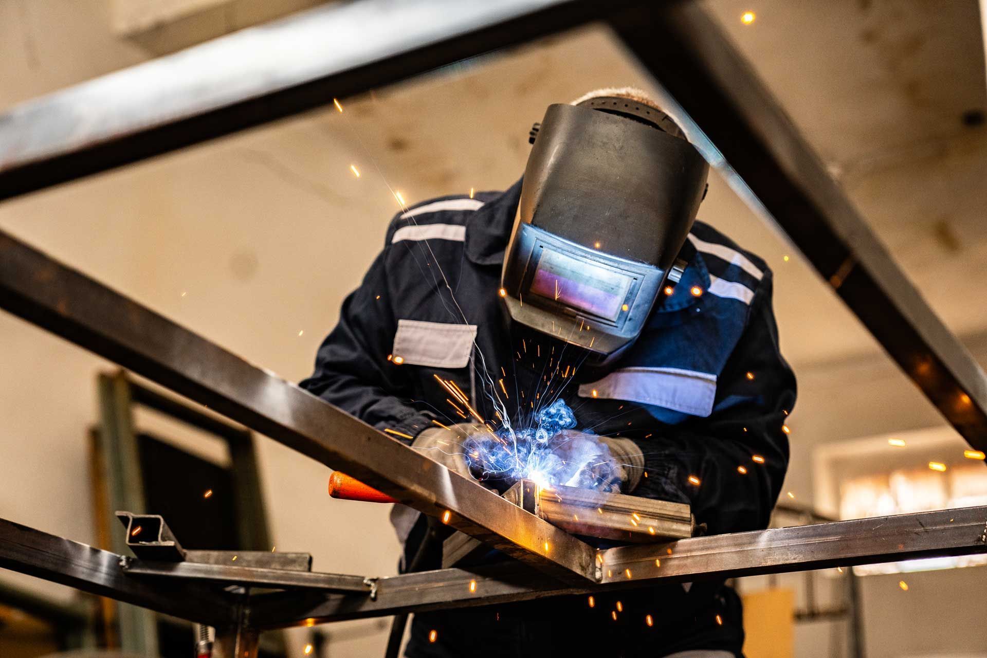 A man is welding a piece of metal in a factory.