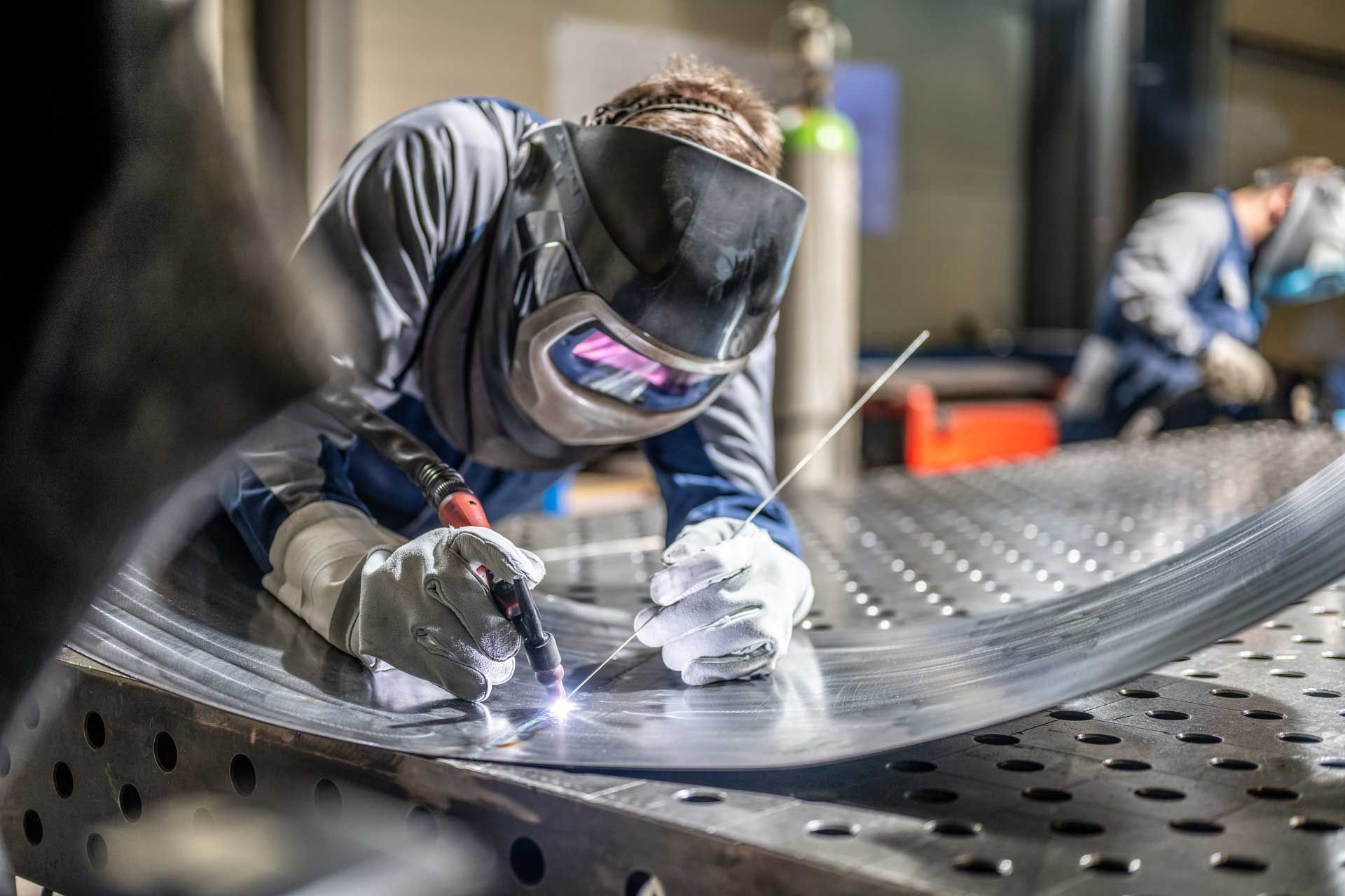 A man is welding a piece of metal in a factory.