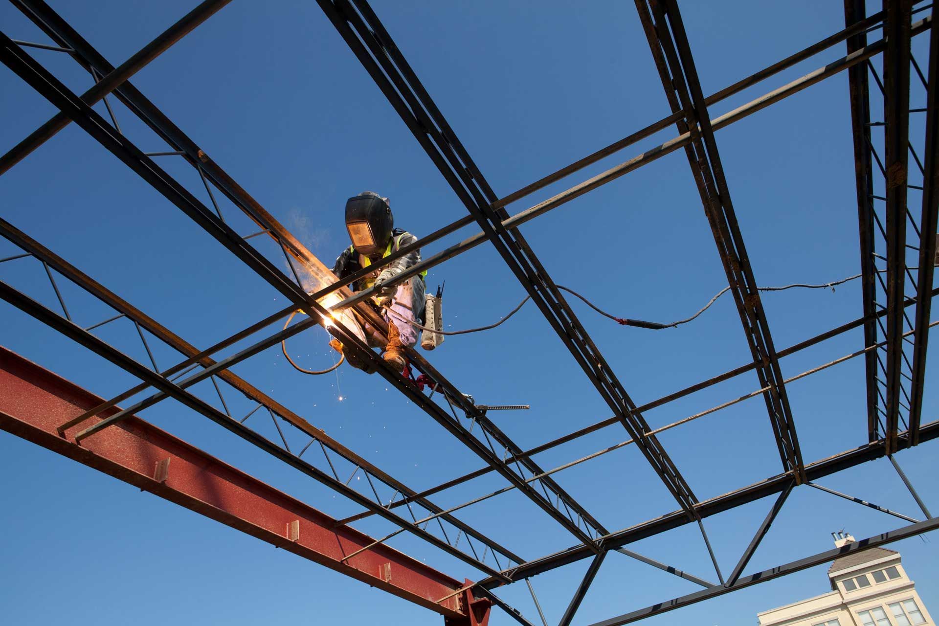 A man is welding a metal structure with a blue sky in the background
