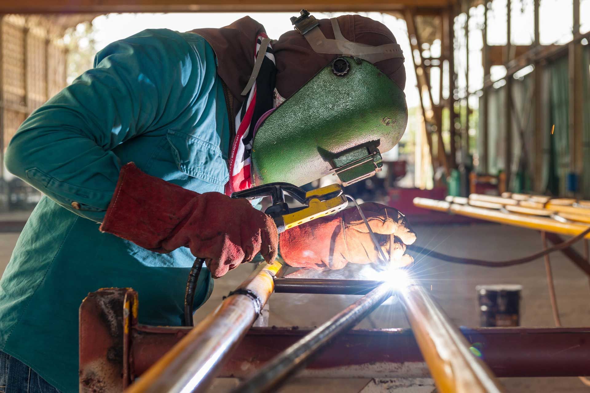 A man is welding a metal pipe in a factory.