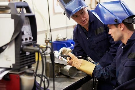 Two men wearing welding helmets are working on a machine in a factory.