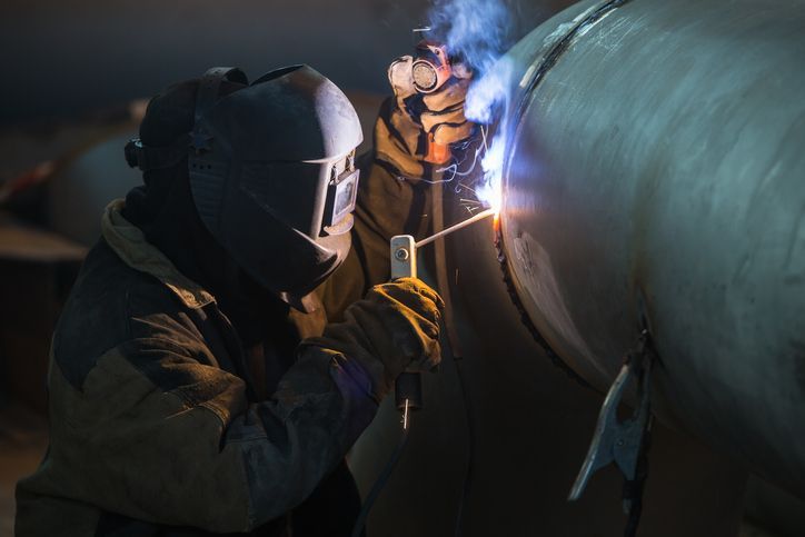 A man wearing a welding mask is welding a pipe.