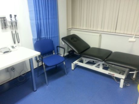 A surgery treatment room with blue carpet, white walls, blue curtain and leather couch
