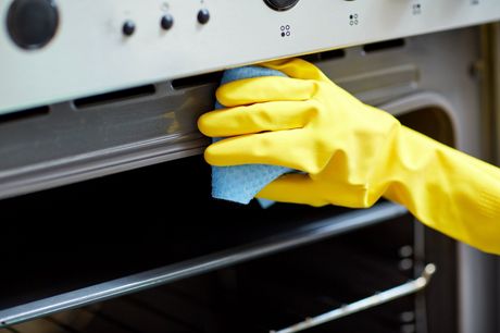 A hand in a yellow rubber glove, cleaning an oven with a blue cloth