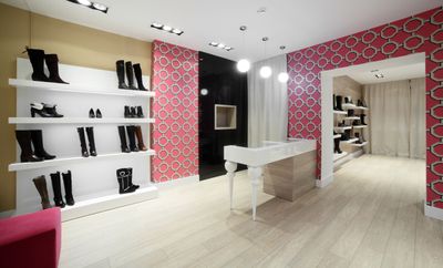 Boots on white shelves in a shoe shop with a pale grey wooden floor and pink feature walls