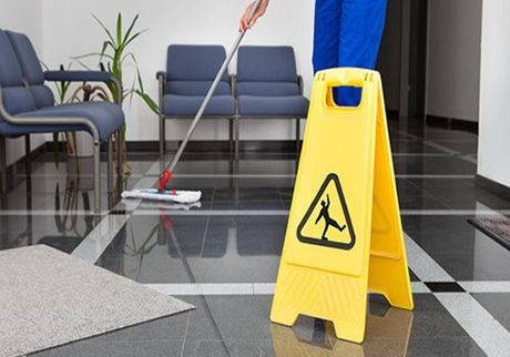 A shiny reception office floor being cleaned behind a yellow safety sign