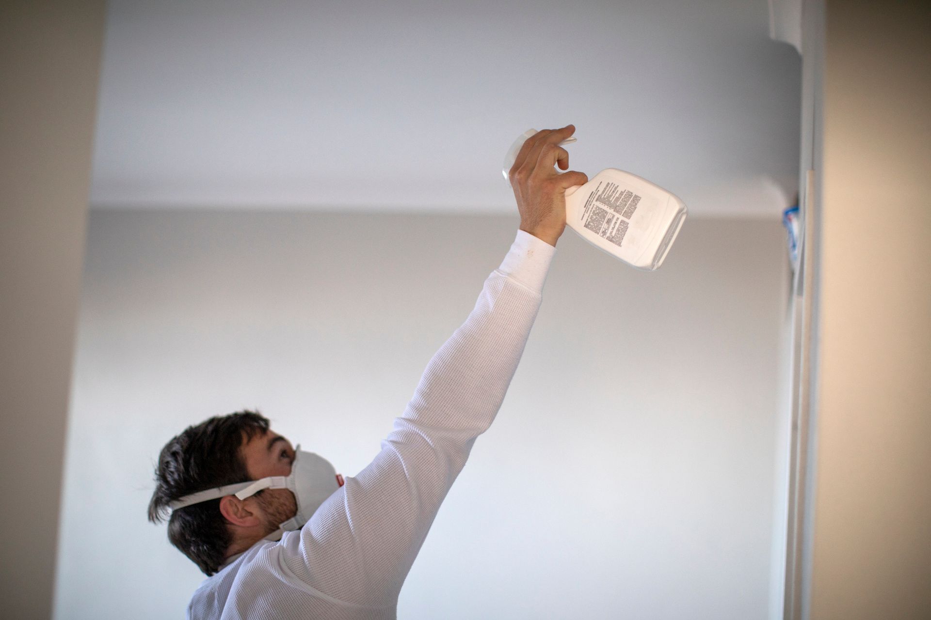 A man wearing a mask is spraying a ceiling with a spray bottle.