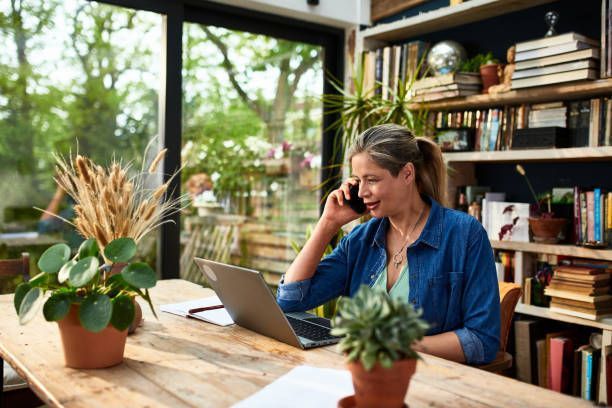 A woman is sitting at a table with a laptop and talking on a cell phone.