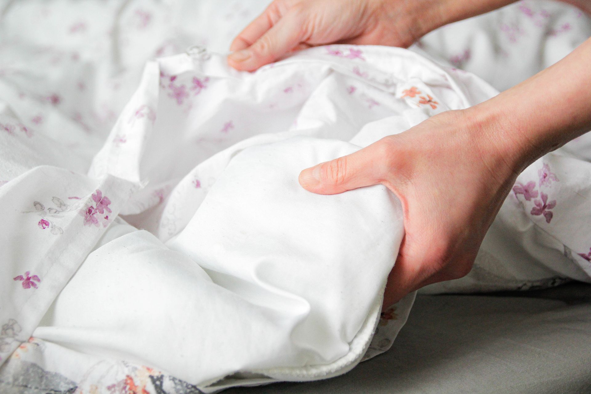 A person is putting a white comforter on a bed.