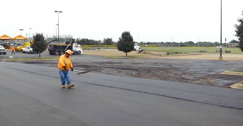 An asphalt paving professional raking aggregate for a new parking lot for a Home Depot.