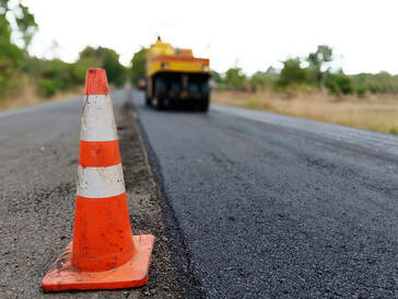 The first image is of an asphalt paver rolling down the street that has freshly installed asphalt on it. An orange road cone sits along the side of the road. The second image is of a brand new, ranch-style home in a residential neighborhood that was just built with fresh asphalt roads. The third image is of a strip mall in Milwaukee with a freshly paved asphalt parking lot.