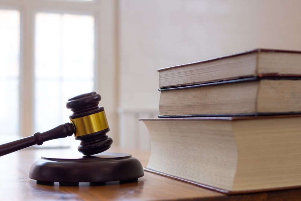 A wooden judge's gavel with a gold band resting on a block next to a small stack of books on a desk.