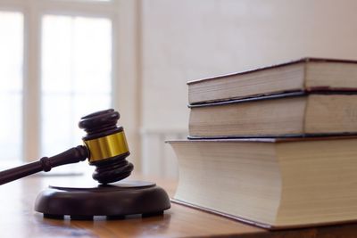 A wooden judge's gavel with a gold band resting on a block next to a small stack of books on a desk.