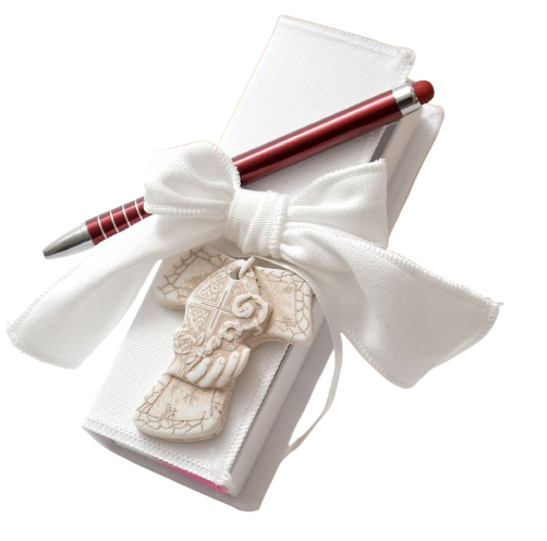 Blocco note con nastro bianco e penna con ciondolo decorativo a forma di croce, forse un regalo per battesimo o religioso.