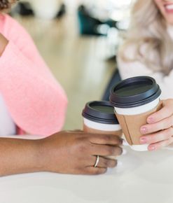 two women sitting at a table holding cups of coffee