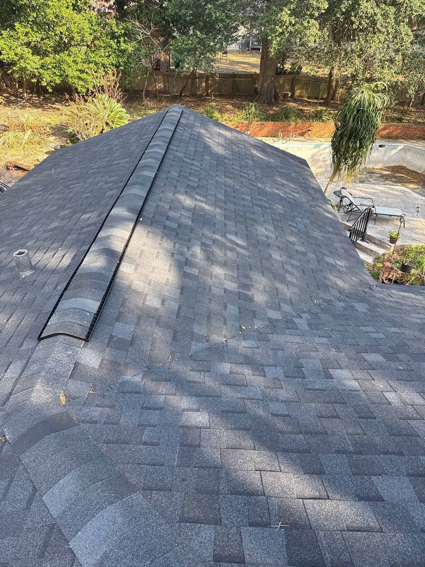 Dark gray shingle roof, ridge vent, sunny outdoor setting with trees and yard.