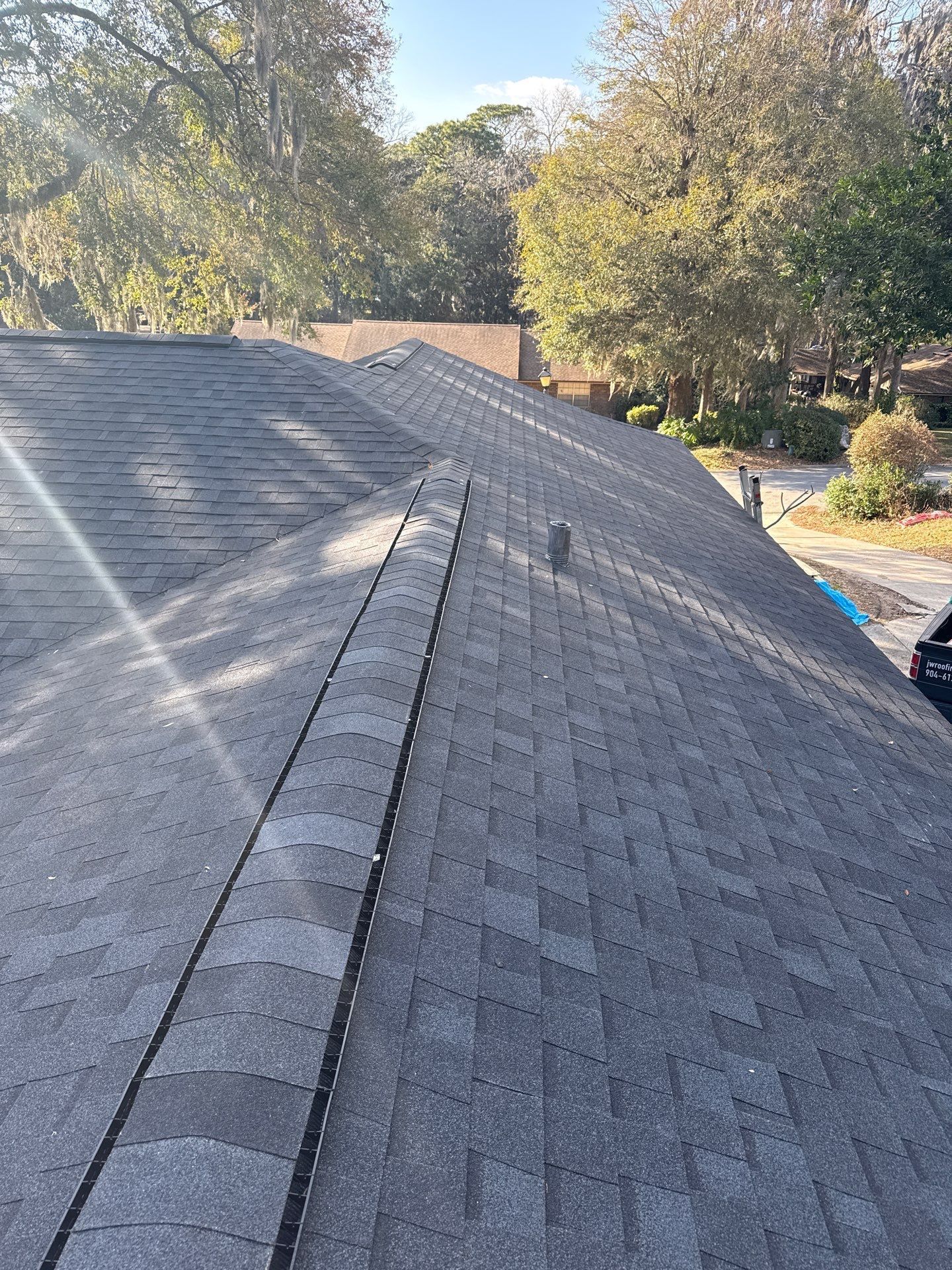 Dark gray shingle roof, with a ridge vent. Trees in background, sunny day.