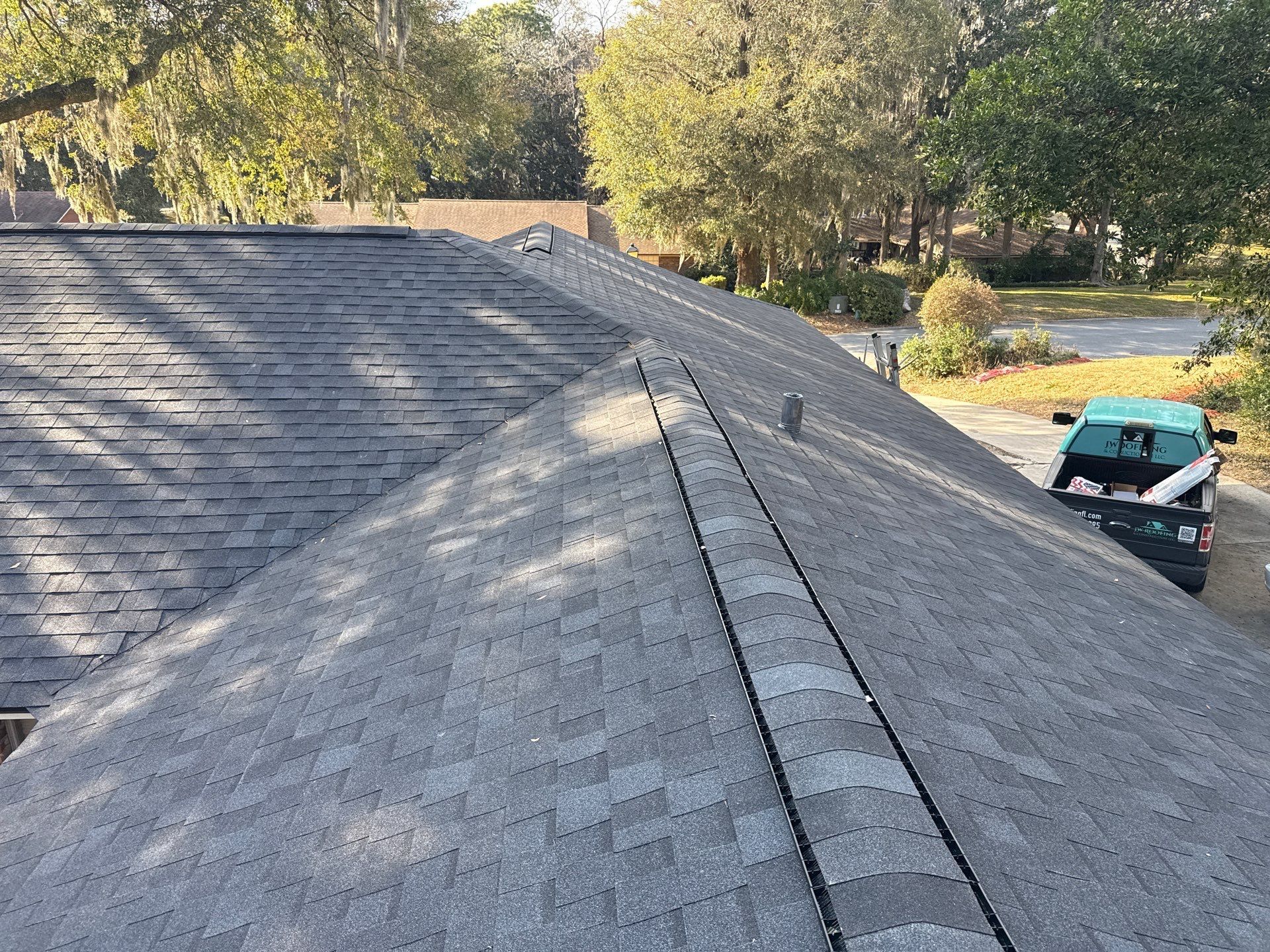 Gray shingle roof, angled view; trees and a green truck in the background.