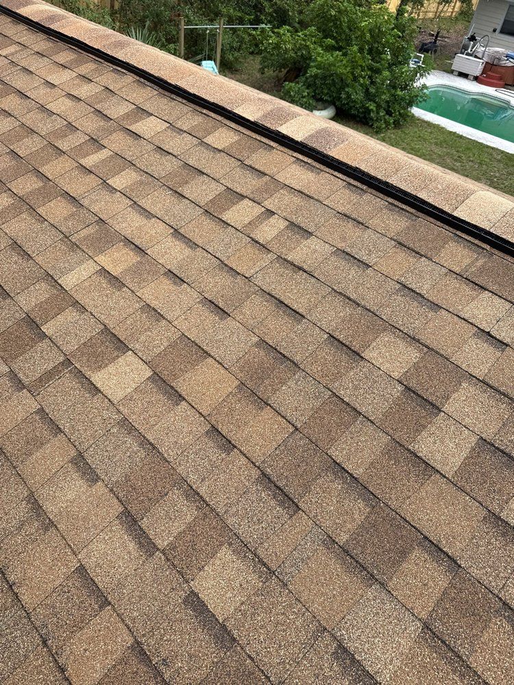 Brown asphalt shingle roof with black ridge cap, outdoors, daylight.