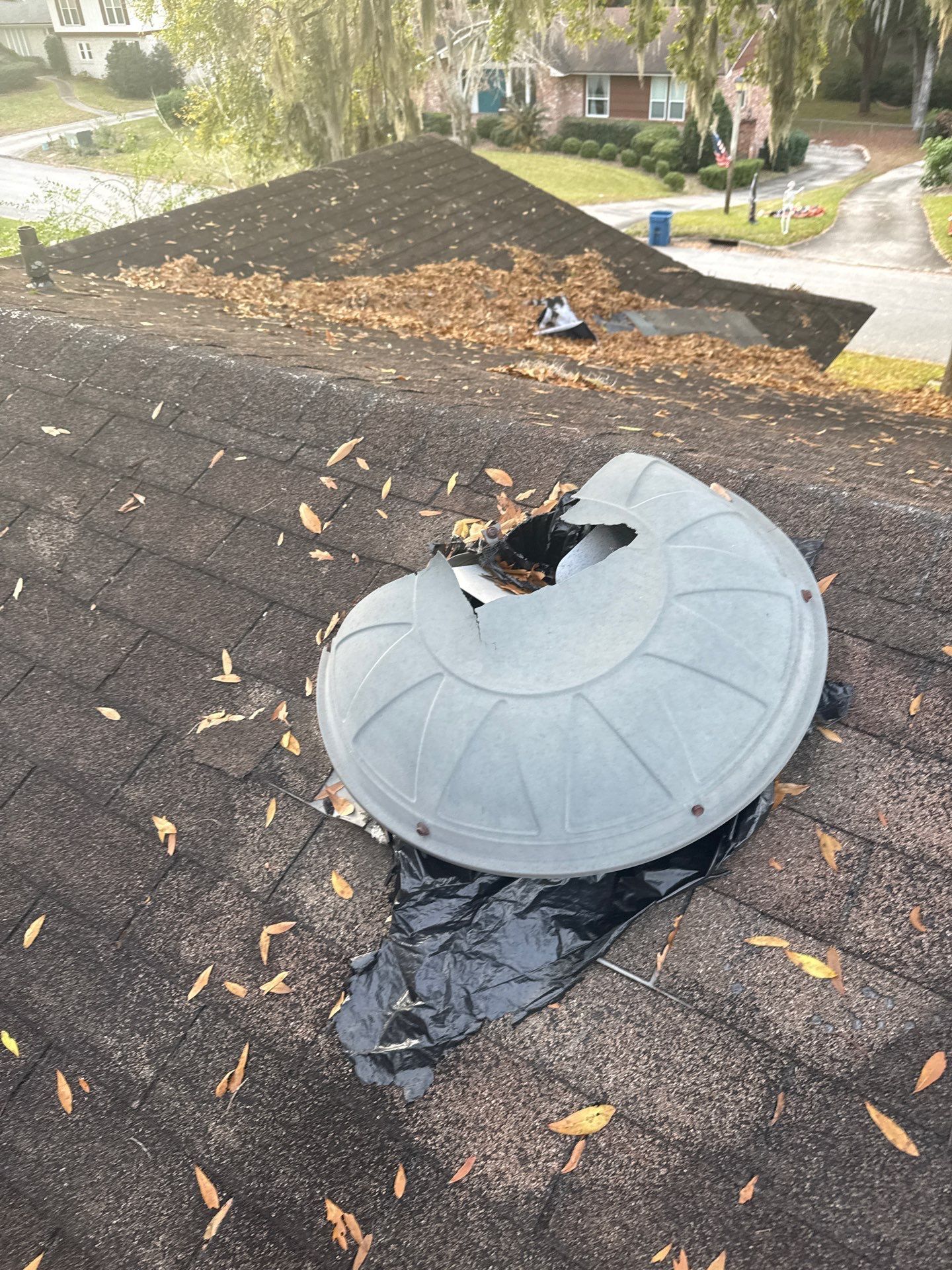 Damaged roof with fallen leaves and a broken ventilation cover.