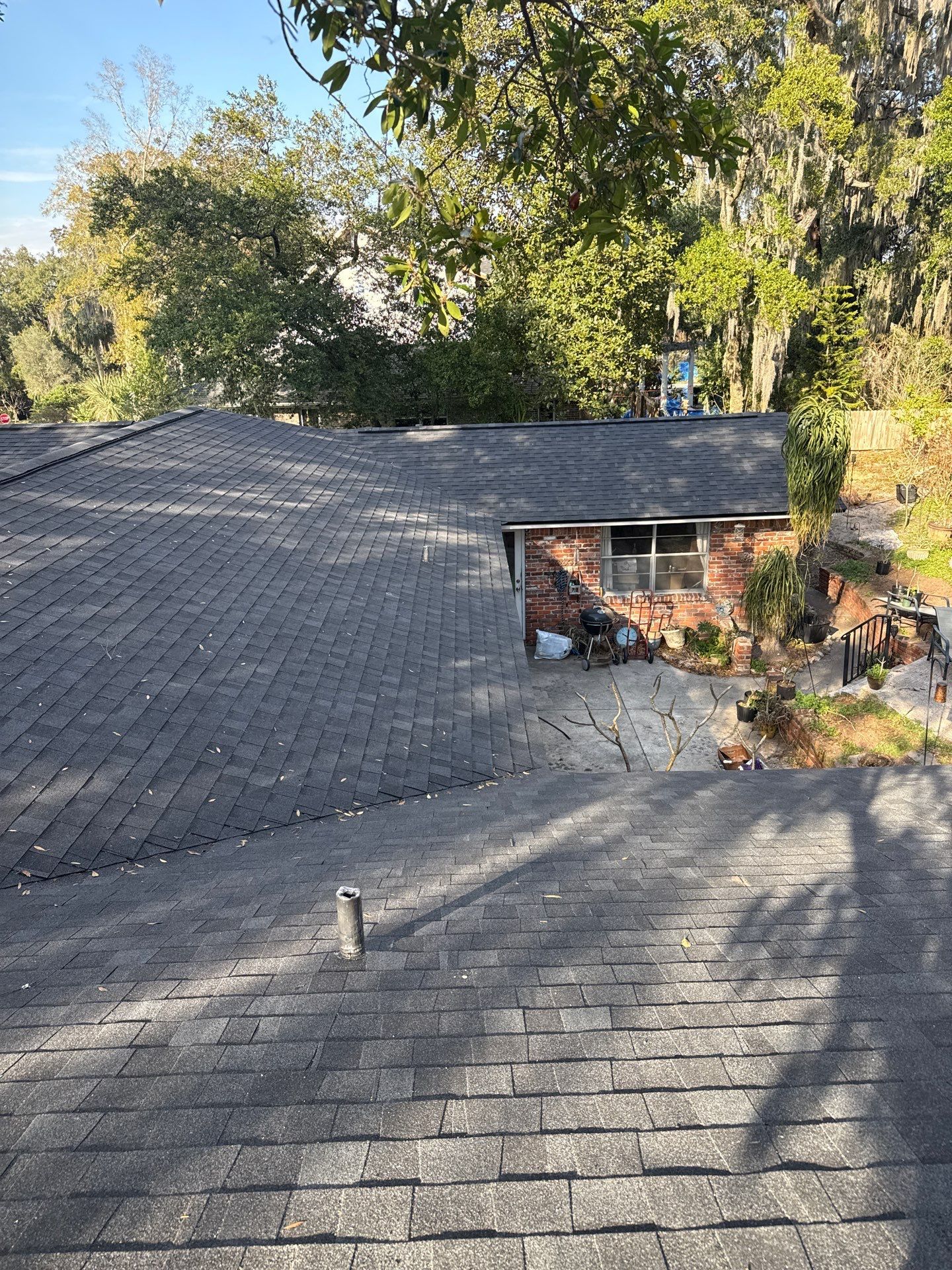 A roof with dark shingles, a vent, and a brick structure. Trees are in the background.