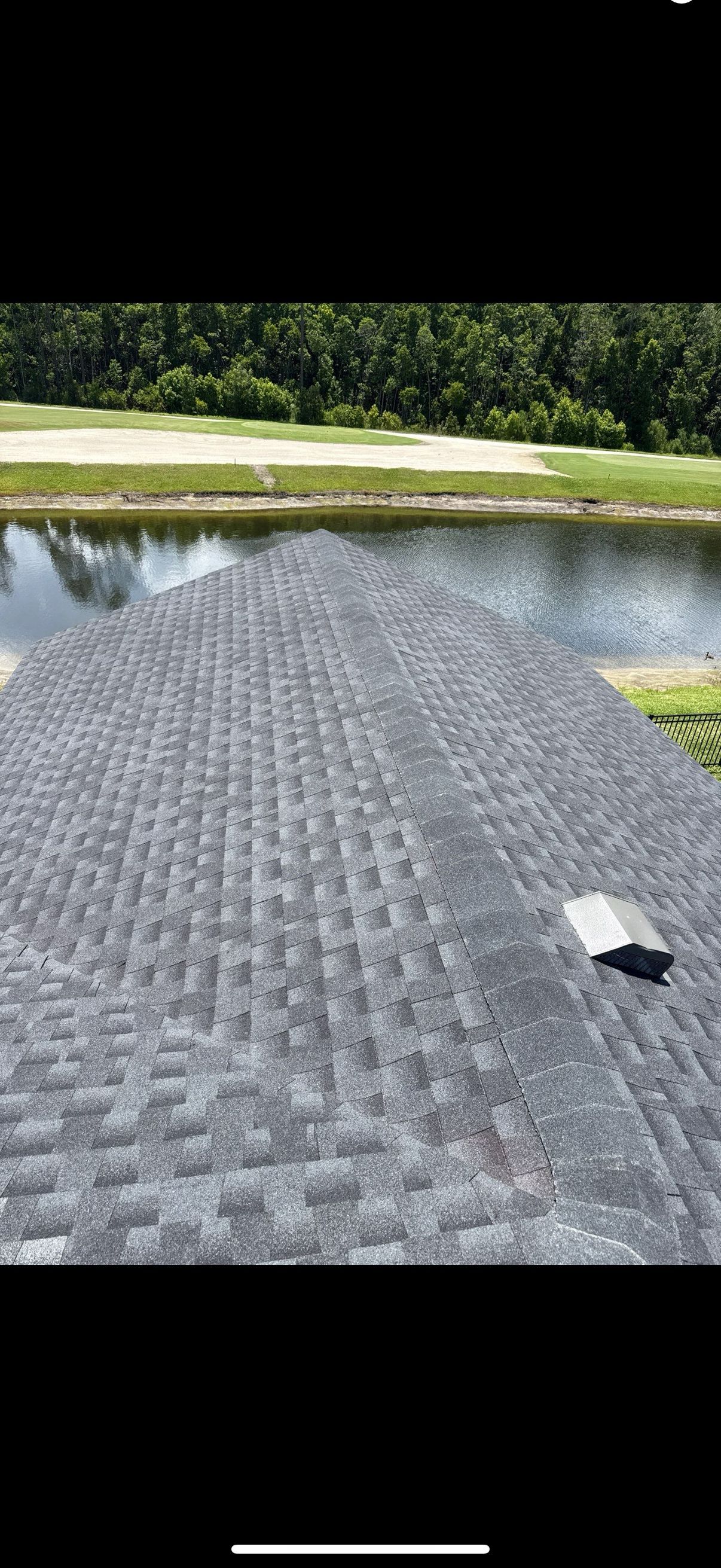 A roof covered in gray asphalt shingles with a water view in the background.