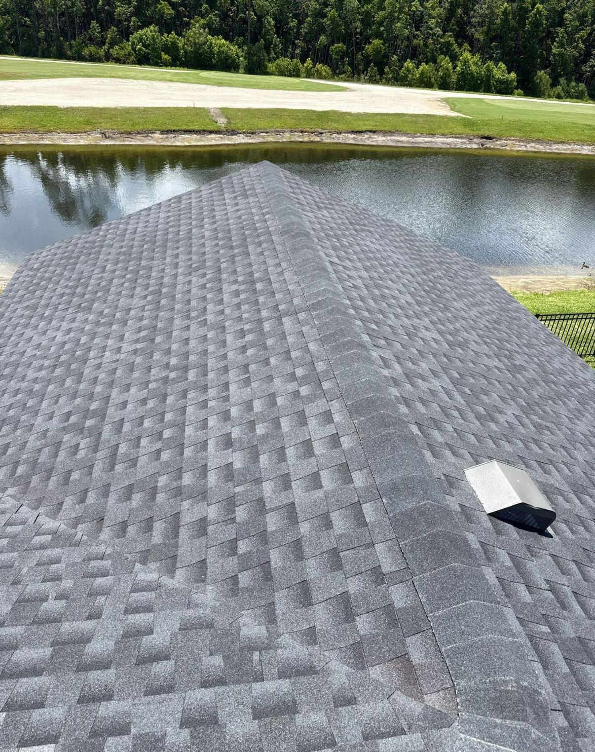 A roof covered in gray asphalt shingles with a water view in the background.