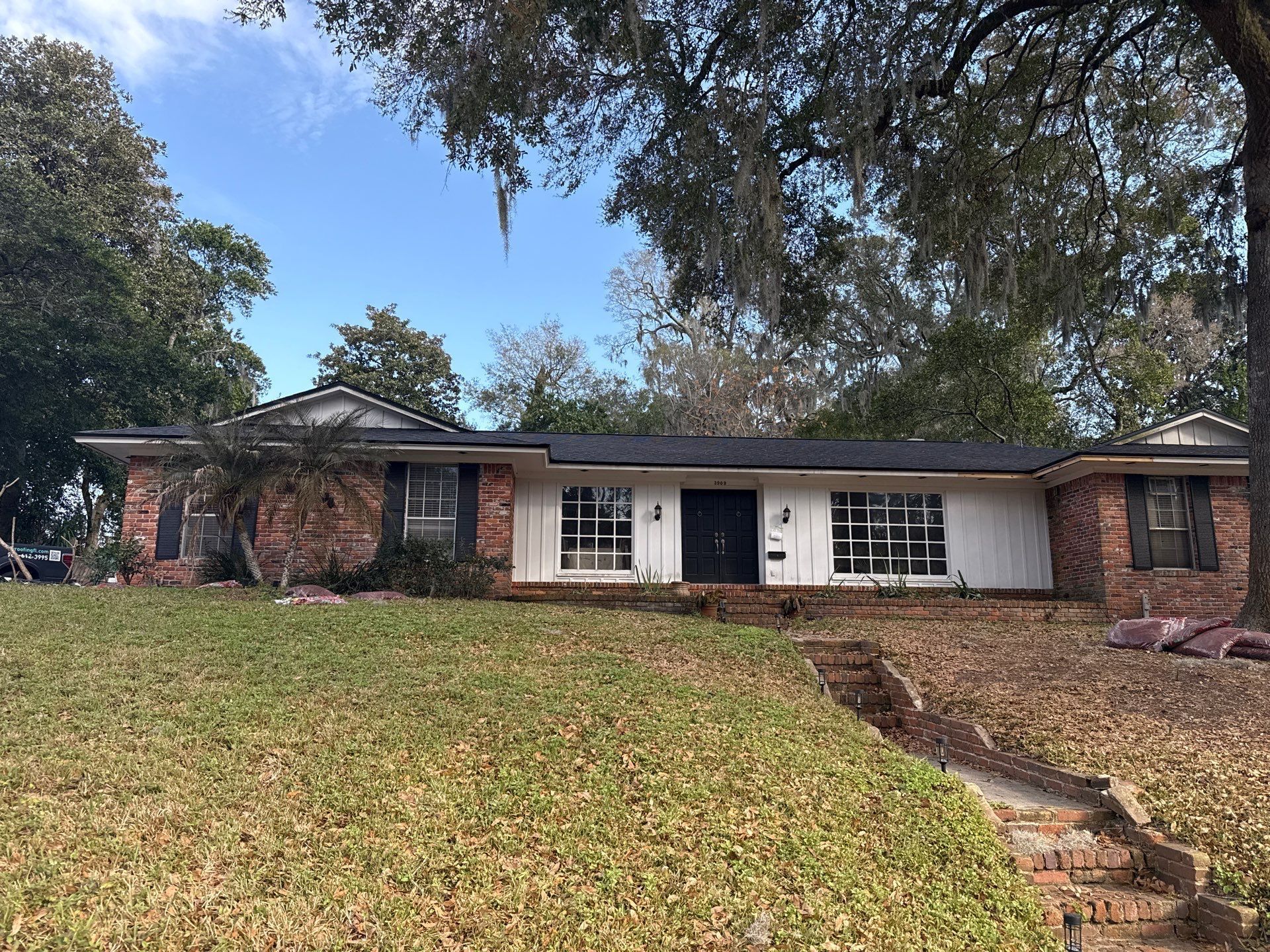 Ranch-style house with brick and white siding, sitting on a grassy hill with a brick pathway.
