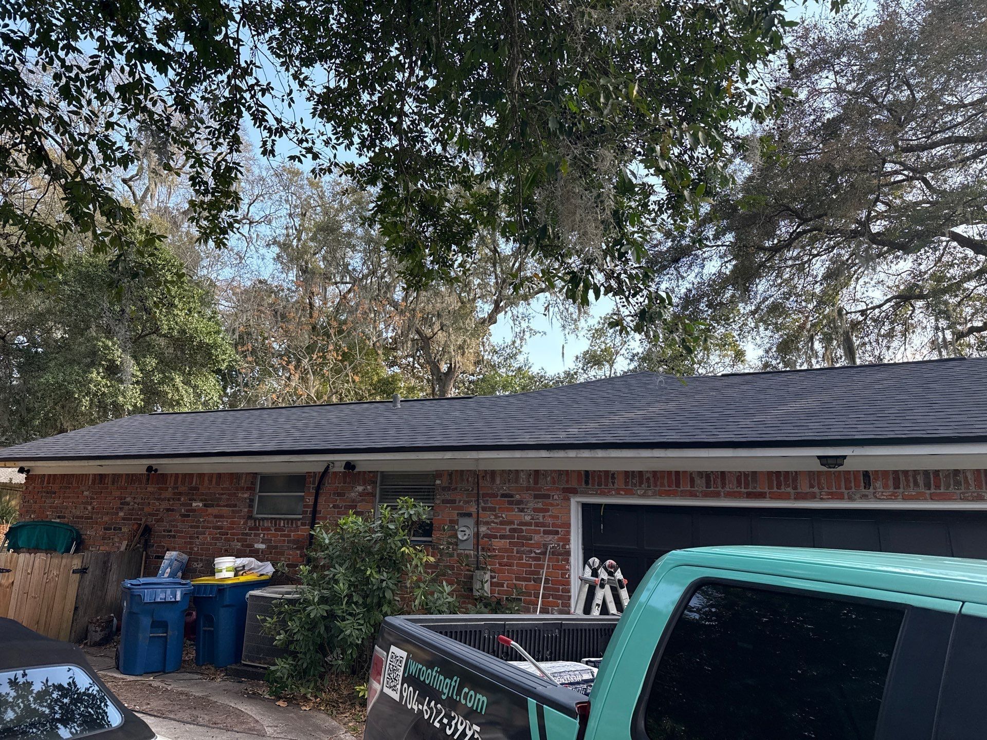 A low-slung, brick building with a dark roof. A turquoise pickup truck is in the foreground. Trees overhead.