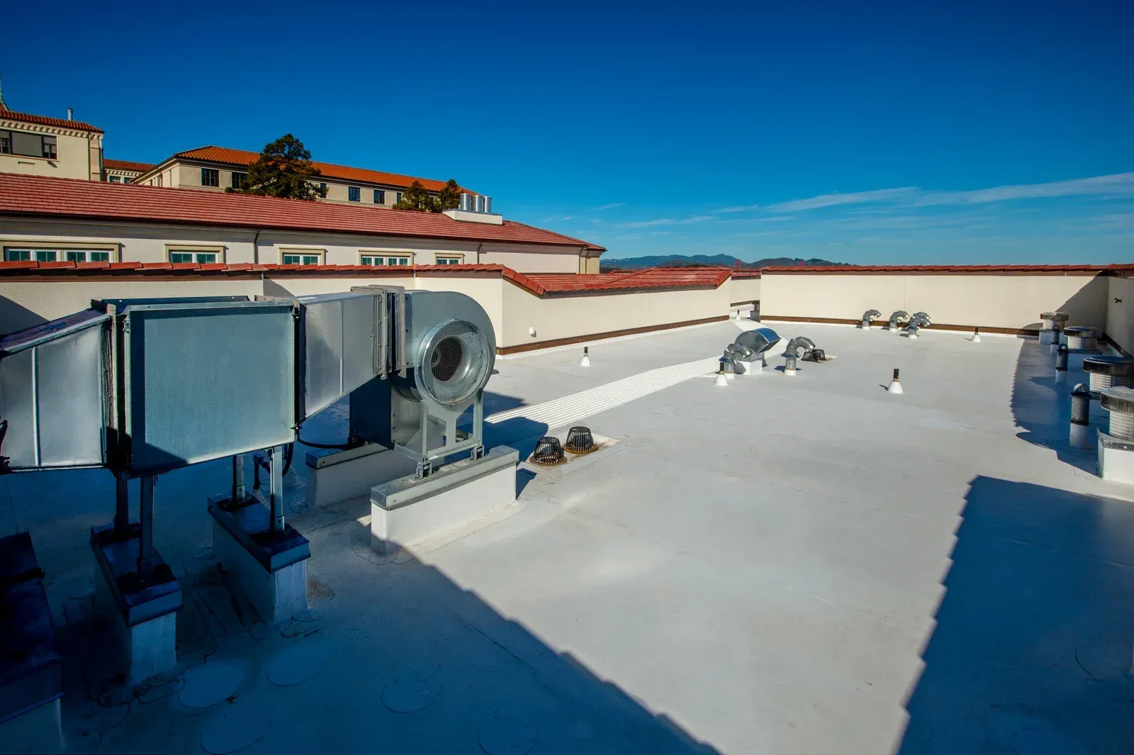 White flat roof with HVAC units under a clear blue sky.