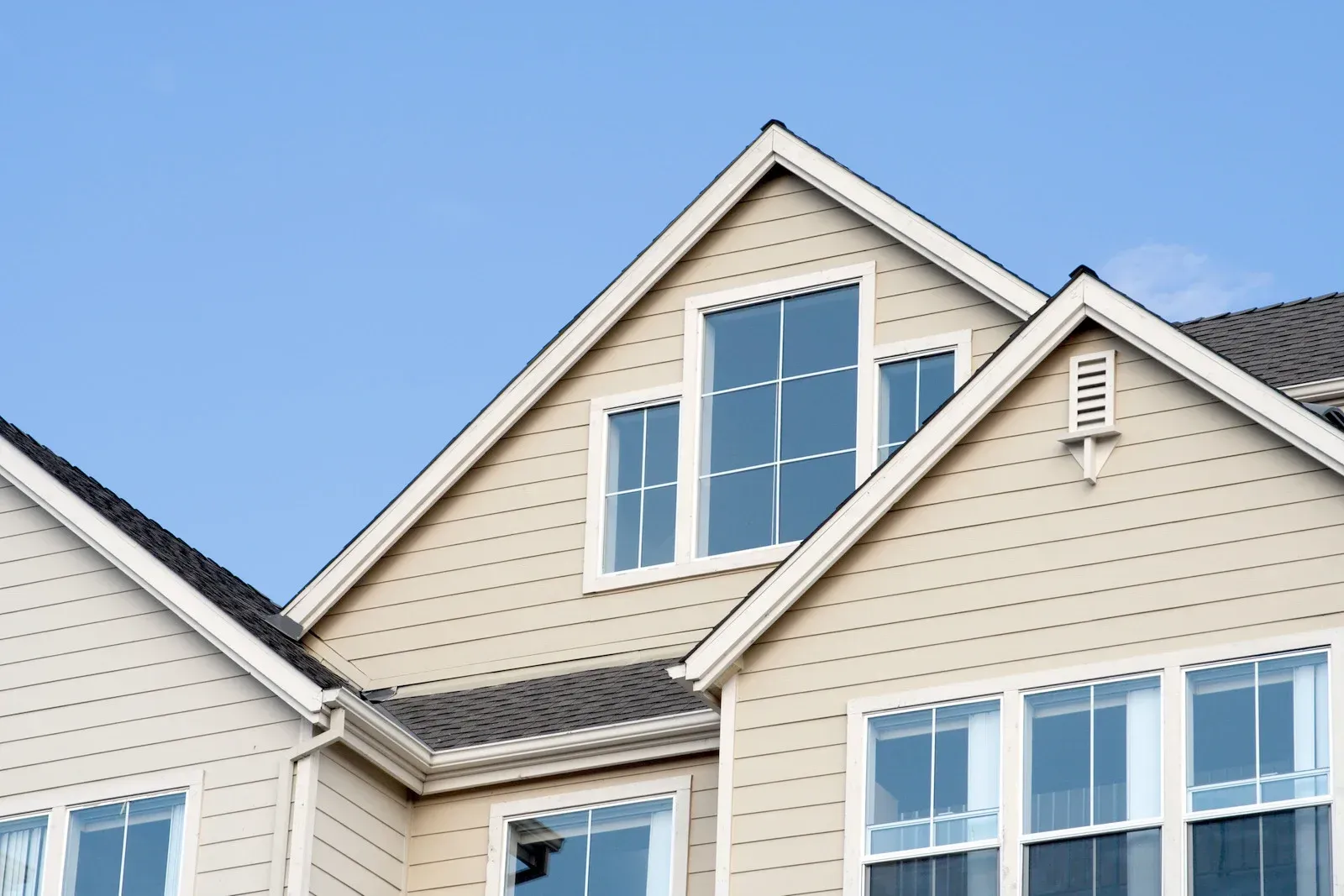 Tan siding house with multiple gabled rooflines and windows against a blue sky.