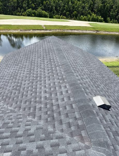 View of a dark gray shingled roof with a water and golf course background.