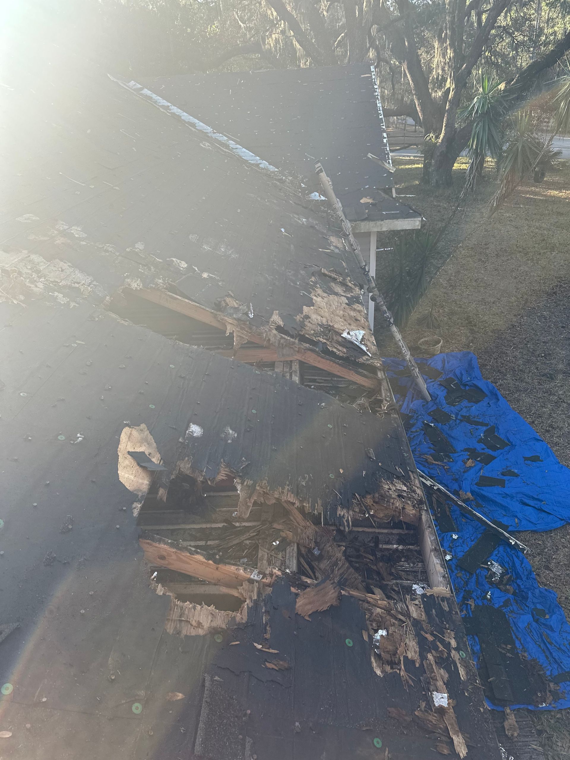 Damaged roof with exposed wood and a blue tarp.
