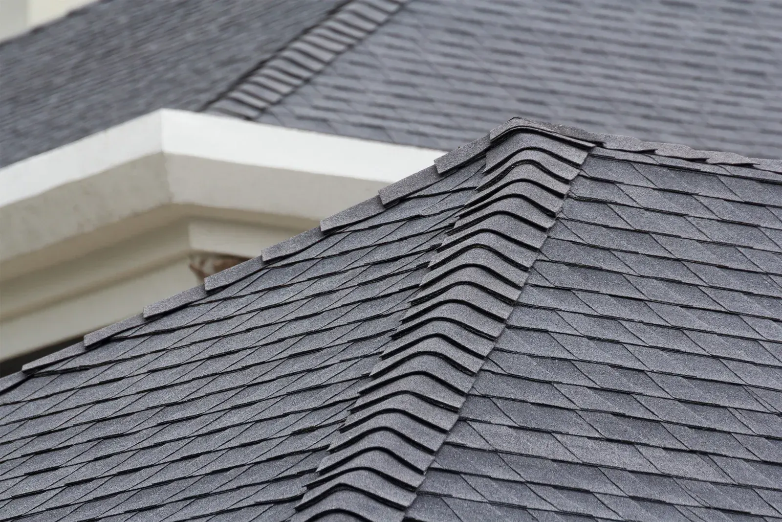 Close-up of a dark gray shingled roof with a white architectural detail in the background.