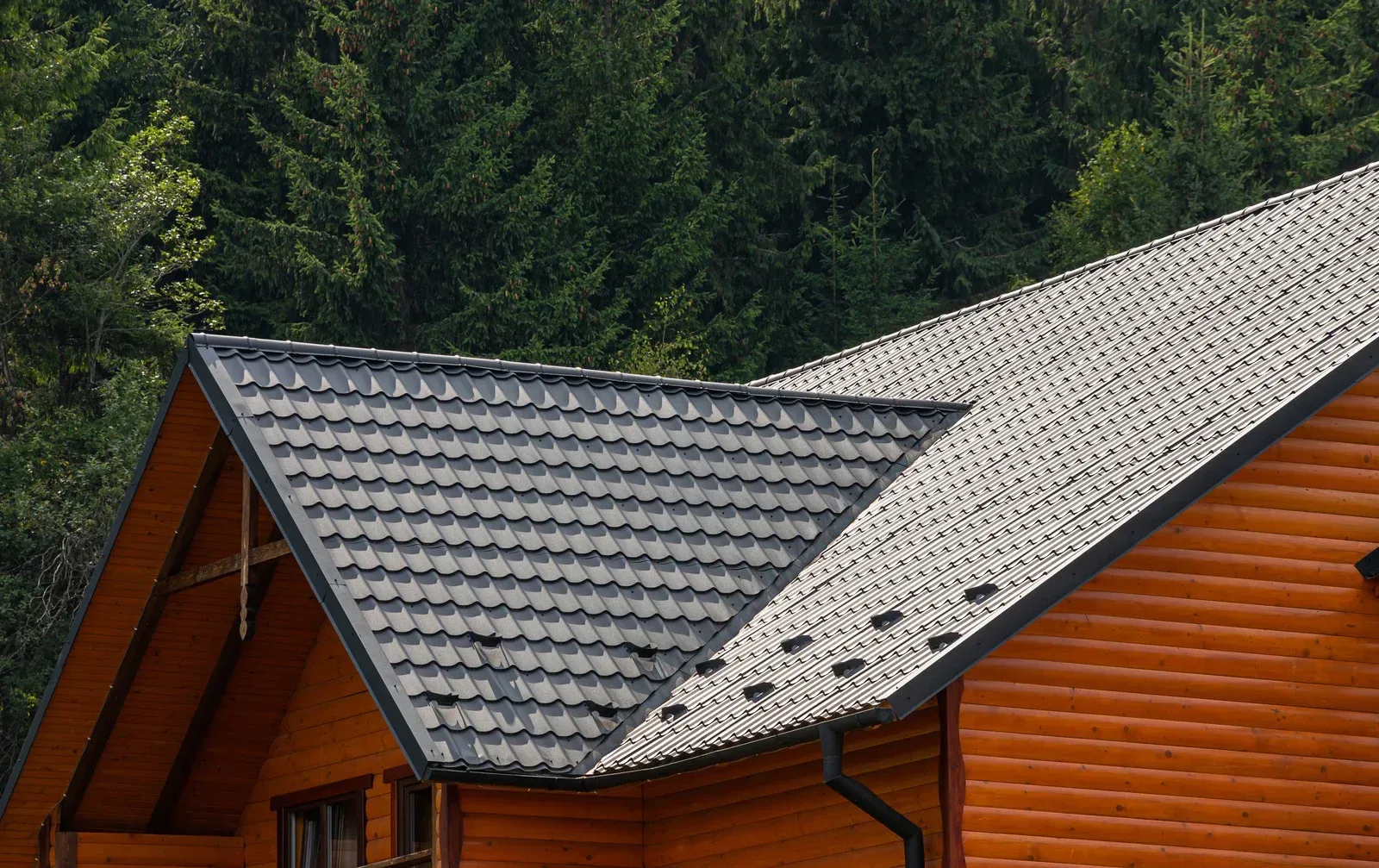Wooden cabin with a dark gray tiled roof, against a backdrop of green trees.