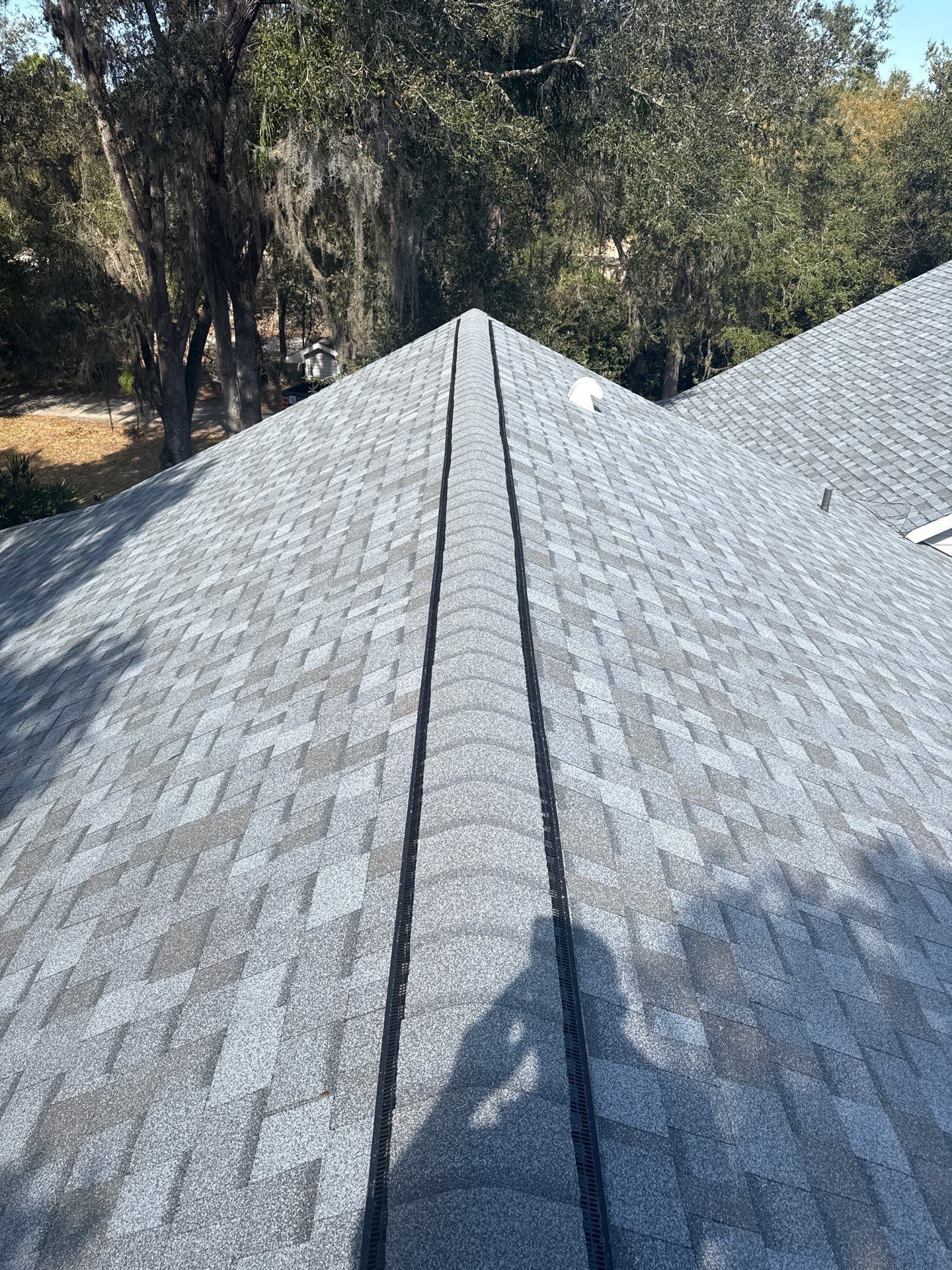 Gray asphalt shingle roof on a house, viewed from above, surrounded by green trees.