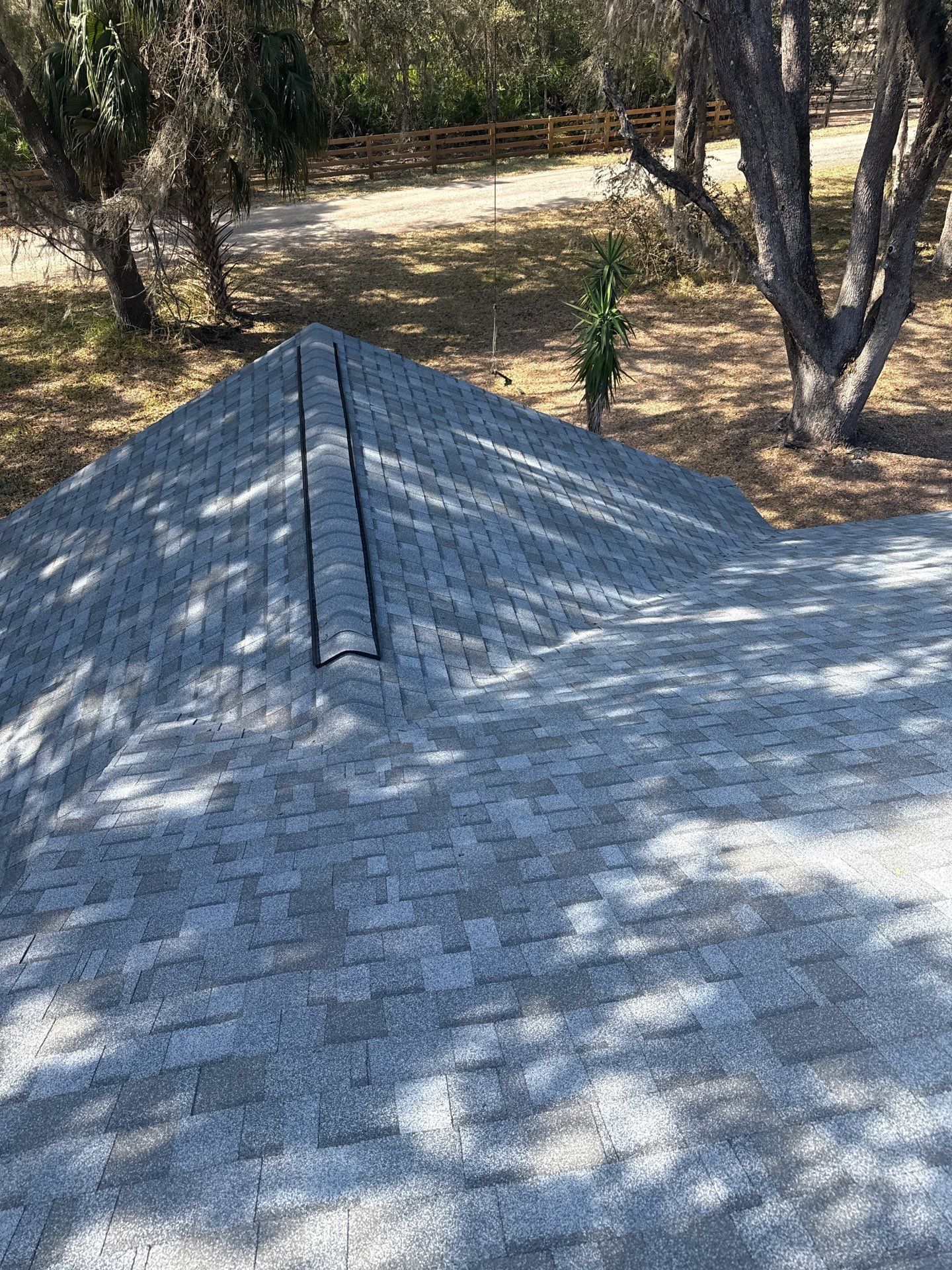 Gray shingle roof, angled view. A black ridge vent runs down the center, with a grassy area in the background.