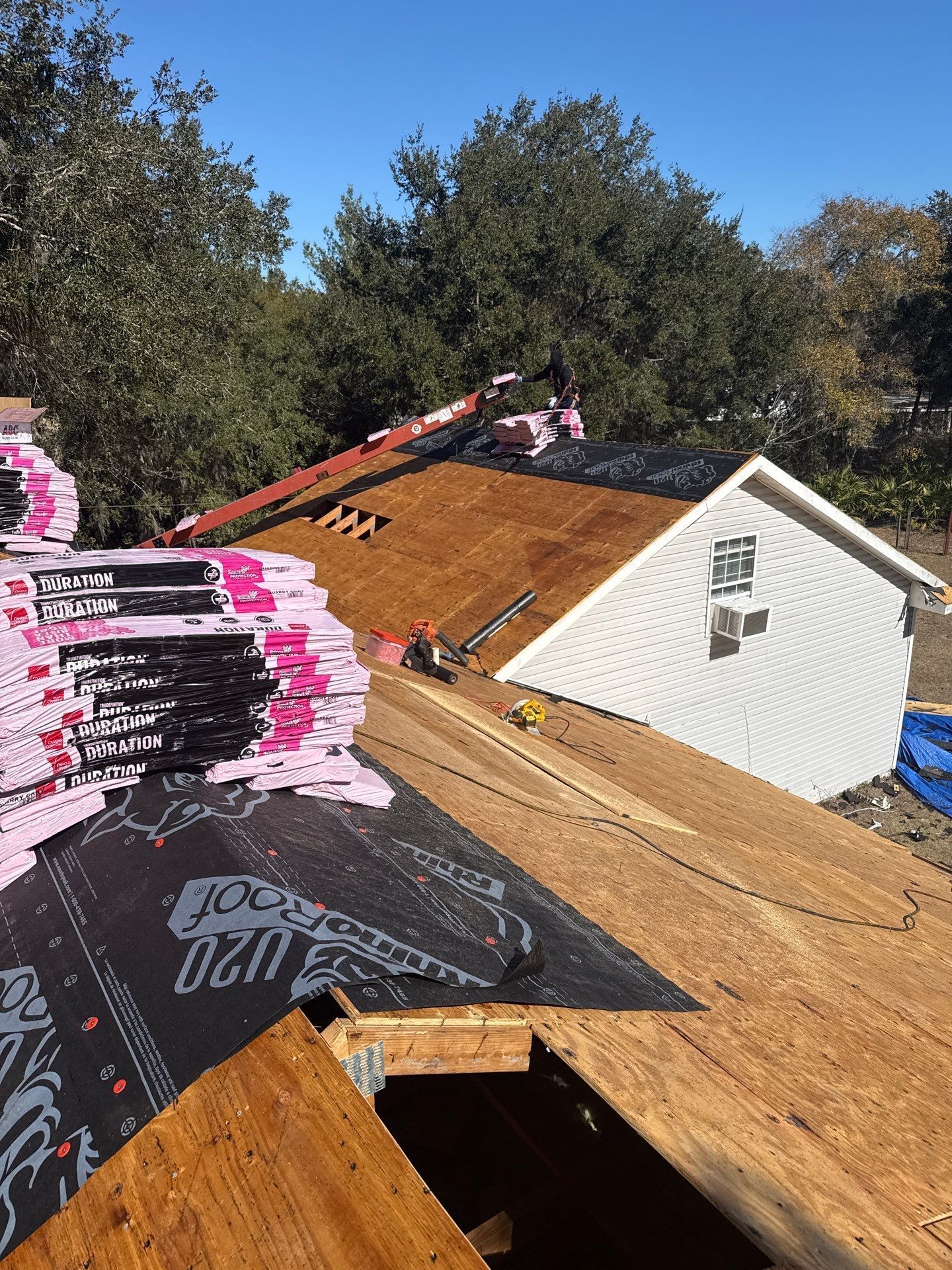 Roof construction: shingles, insulation, and lumber on a rooftop, with a small white building nearby.
