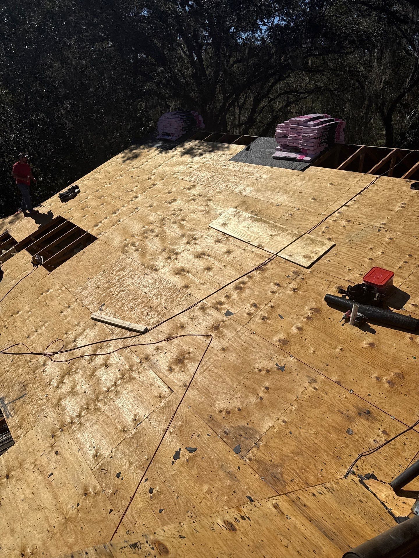 Roof being worked on, plywood covered with scattered materials, two workers visible.