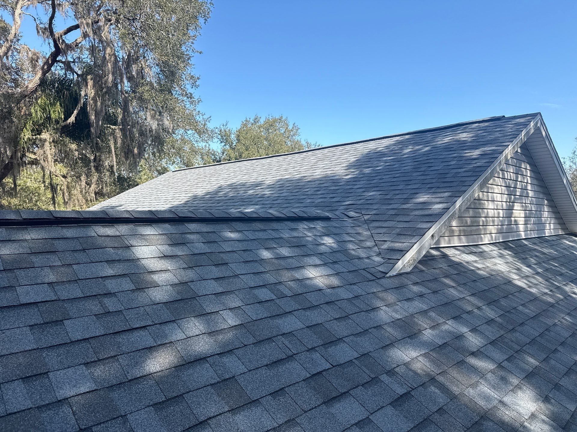 Gray shingled roof under a clear blue sky, with a wooden gable.