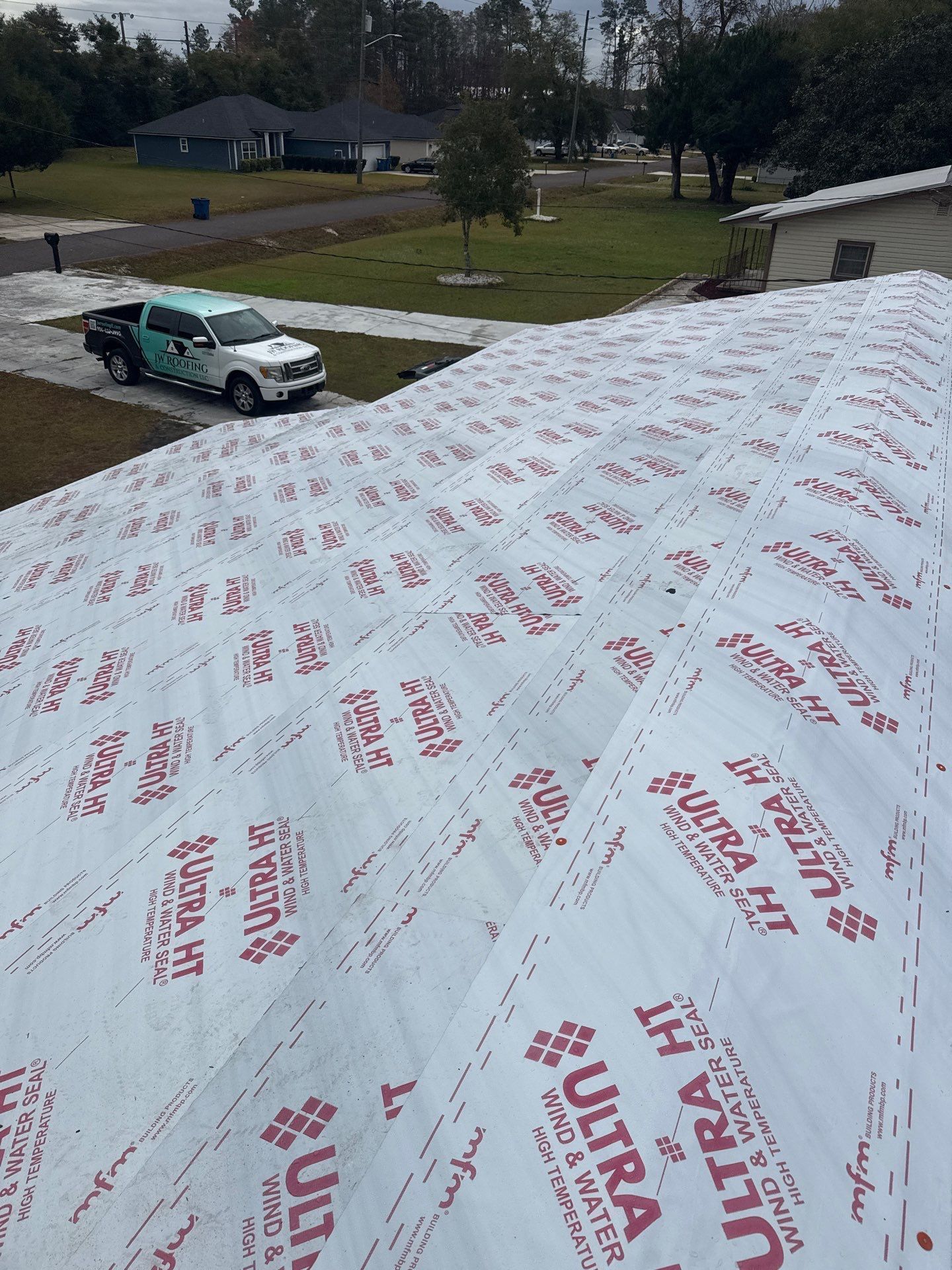White underlayment with red text covers a roof, truck parked nearby.