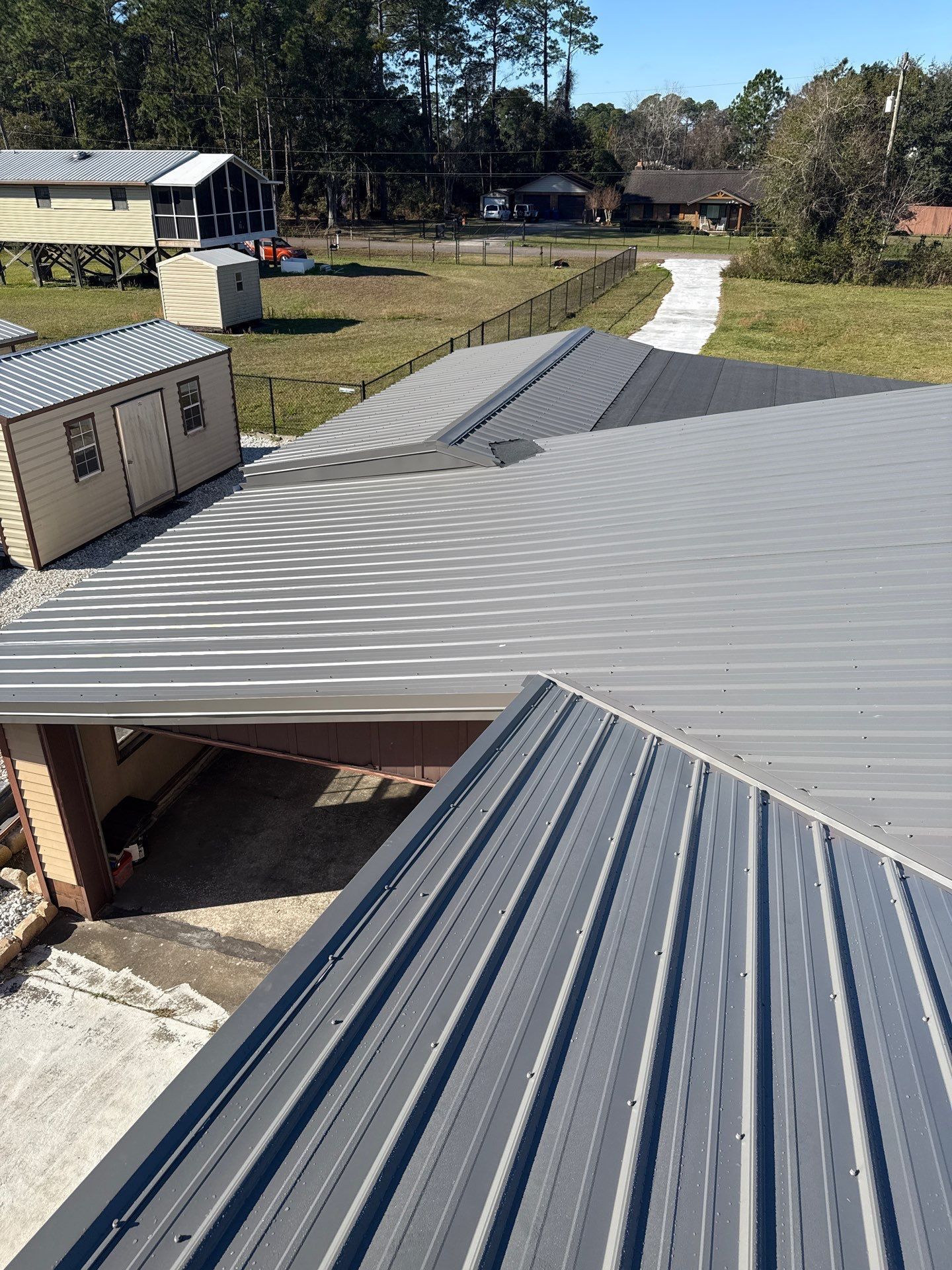 Overhead view of a gray metal roof on a residential building with a path and trees in the background.
