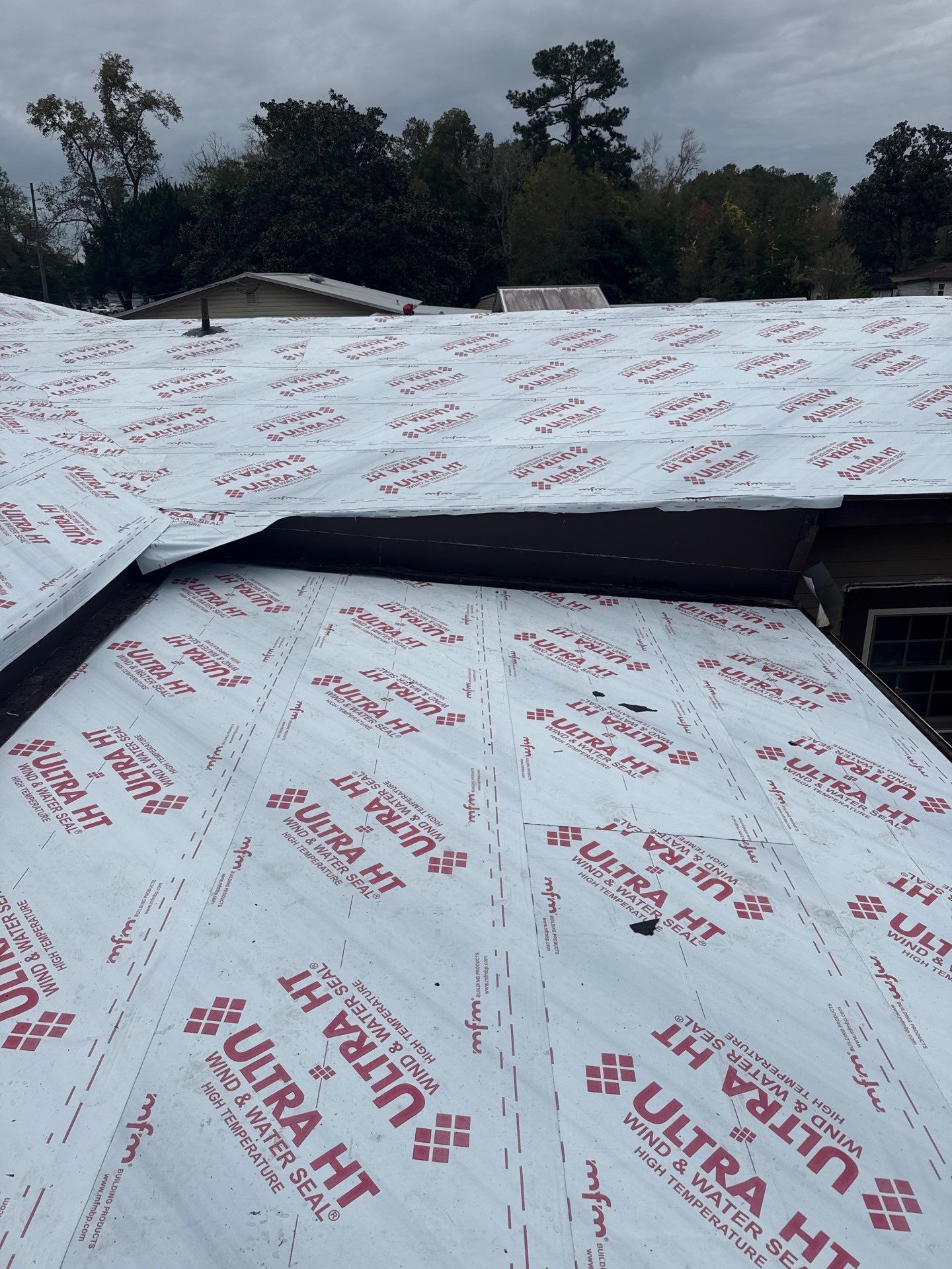 Roof under construction, covered in white roofing underlayment with red and black text.